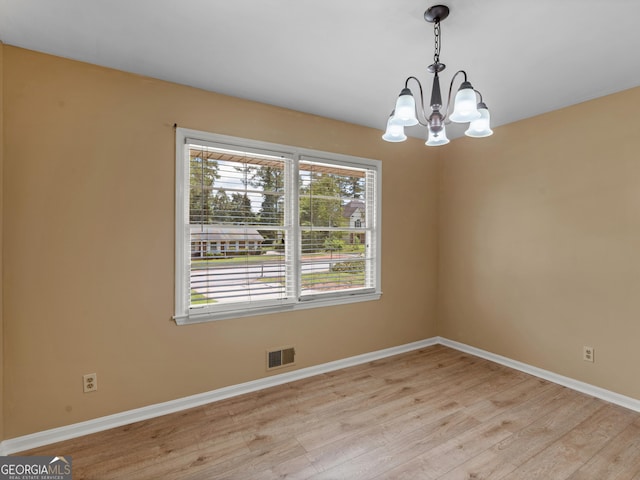 spare room featuring baseboards, visible vents, an inviting chandelier, and light wood finished floors