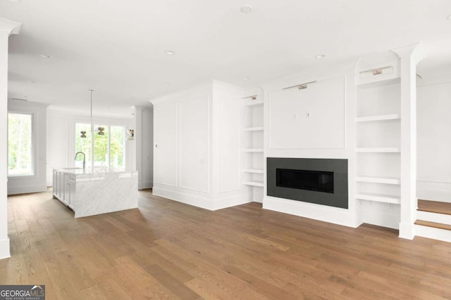 11542 Serenbe Ln, Chattahoochee Hills, GA 30268 - unfurnished living room with a sink, a glass covered fireplace, built in features, baseboards, and wood finished floors