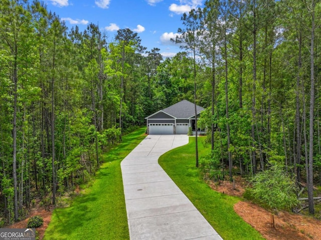 view of front facade with concrete driveway, a garage, a wooded view, and a front lawn