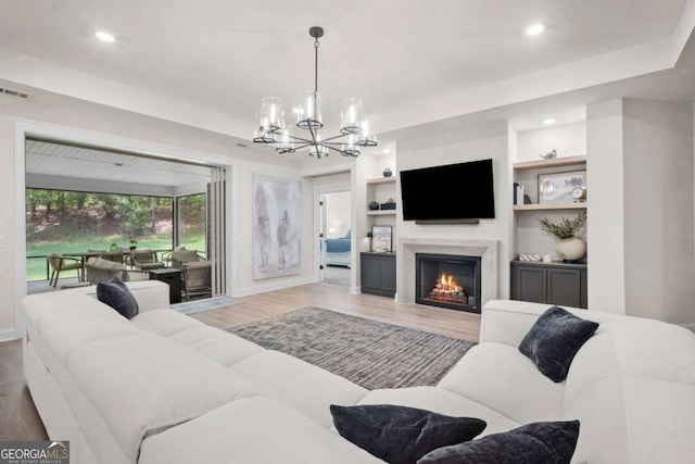 living area with recessed lighting, a lit fireplace, light wood-type flooring, and a notable chandelier