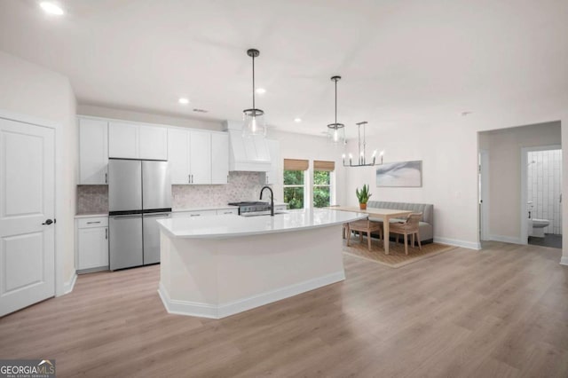 kitchen with white cabinets, a sink, light countertops, premium range hood, and freestanding refrigerator