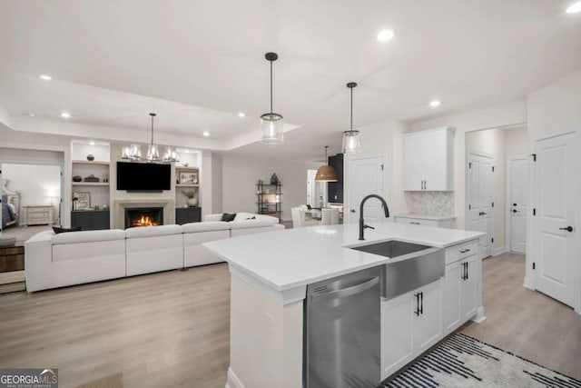 kitchen with stainless steel dishwasher, a kitchen island with sink, open floor plan, a sink, and light wood finished floors