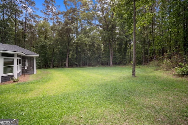 view of yard with a sunroom and a wooded view