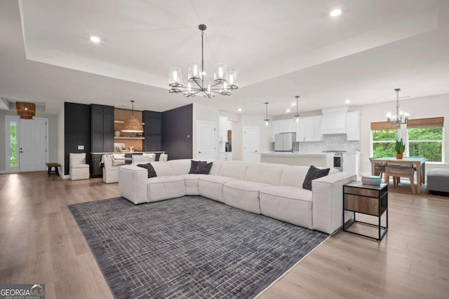 living area featuring an inviting chandelier, light wood-style flooring, a tray ceiling, and a healthy amount of sunlight