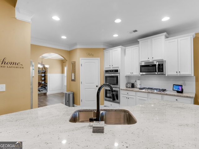 kitchen with crown molding, appliances with stainless steel finishes, arched walkways, a sink, and white cabinets