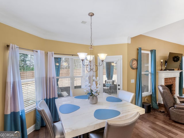 dining area with crown molding, a brick fireplace, wood finished floors, and a chandelier