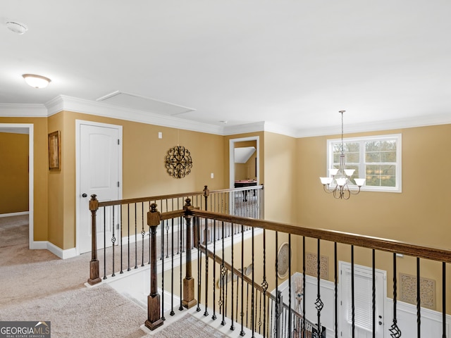 corridor featuring carpet flooring, a chandelier, attic access, an upstairs landing, and ornamental molding