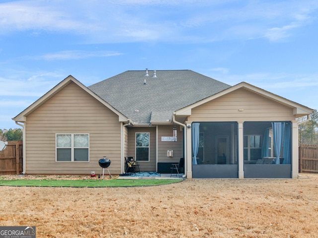 rear view of property featuring fence, a shingled roof, and a sunroom