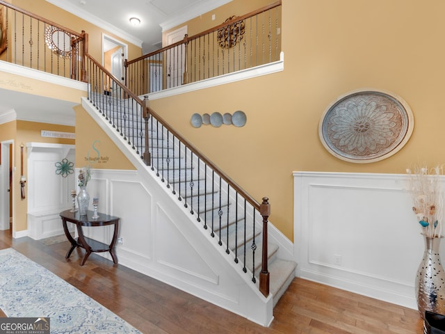 staircase featuring crown molding, wainscoting, a decorative wall, and wood finished floors