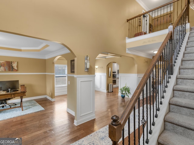 stairs with wainscoting, arched walkways, ornamental molding, and wood finished floors
