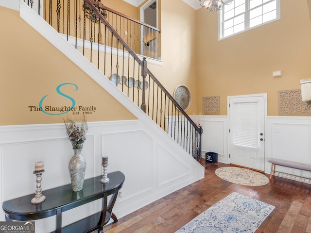 entryway featuring an inviting chandelier, a decorative wall, a wainscoted wall, a towering ceiling, and stairway