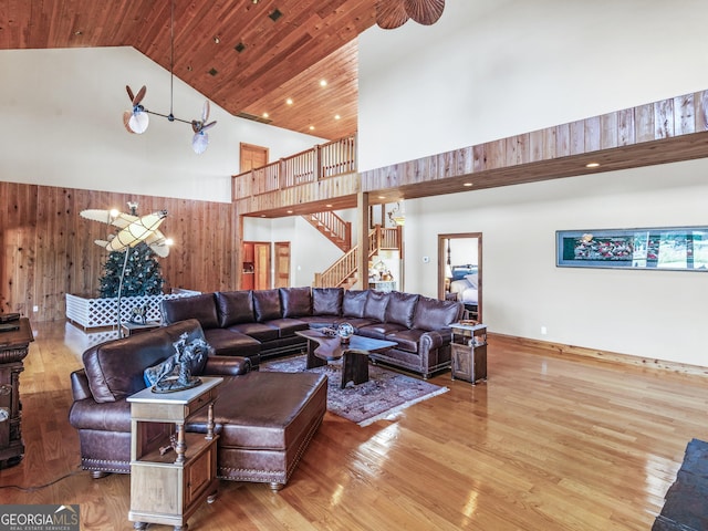 living room with high vaulted ceiling, wood walls, stairs, and wood finished floors