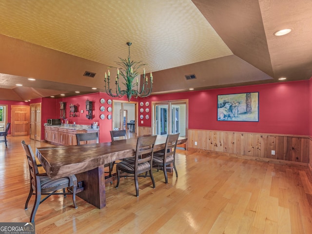 dining area with a notable chandelier, light wood-style floors, a wainscoted wall, vaulted ceiling, and visible vents