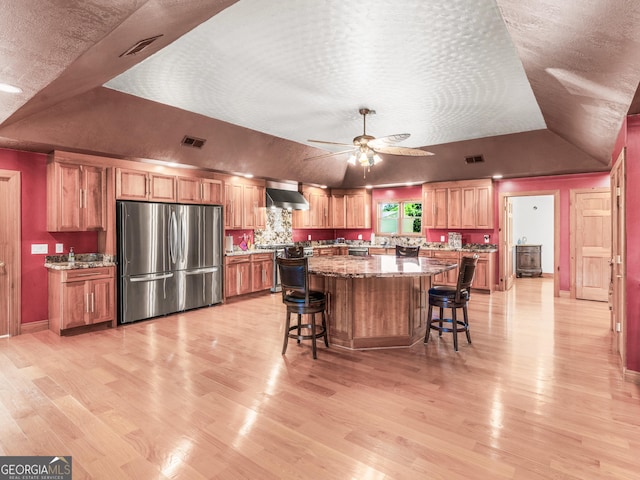 kitchen featuring a kitchen breakfast bar, visible vents, a center island, freestanding refrigerator, and lofted ceiling