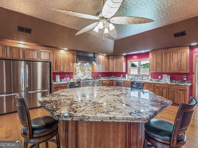 kitchen featuring visible vents, appliances with stainless steel finishes, brown cabinetry, and wall chimney exhaust hood