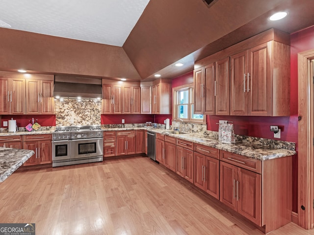 kitchen with light stone countertops, appliances with stainless steel finishes, a sink, light wood-style flooring, and wall chimney exhaust hood