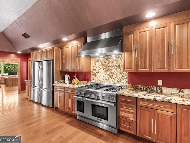 kitchen with visible vents, brown cabinets, light wood-style floors, stainless steel appliances, and wall chimney exhaust hood