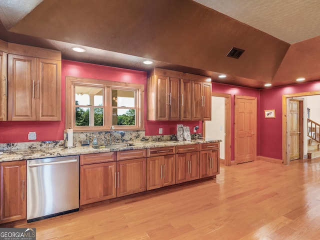 kitchen featuring brown cabinetry, light wood-type flooring, dishwasher, a sink, and light stone counters
