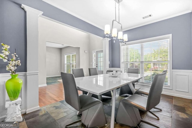 dining space featuring crown molding, visible vents, wainscoting, stone finish floor, and a notable chandelier