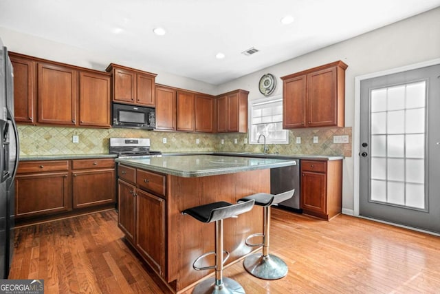 kitchen featuring dark wood-style flooring, a sink, stainless steel appliances, a kitchen island, and visible vents