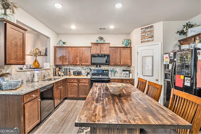kitchen featuring a sink, tasteful backsplash, light stone counters, black appliances, and light wood-type flooring