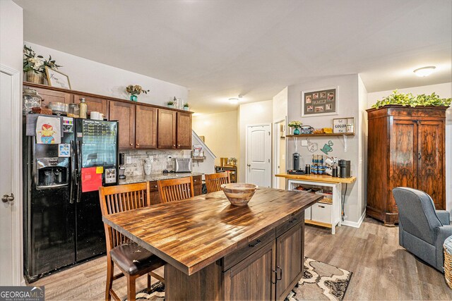 kitchen with wood counters, light wood finished floors, decorative backsplash, and black fridge with ice dispenser