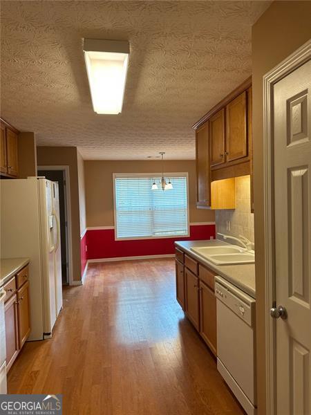 3218 Watson Woods Way, Loganville, GA 30052 - kitchen featuring a sink, light wood finished floors, brown cabinetry, and white appliances