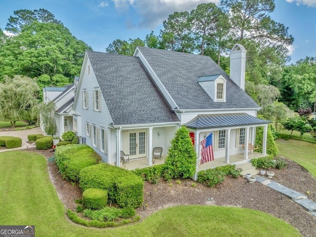 rear view of property featuring covered porch, french doors, a chimney, a lawn, and a shingled roof