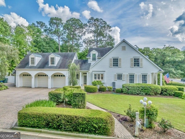 cape cod home featuring roof with shingles, an attached garage, decorative driveway, and a front lawn