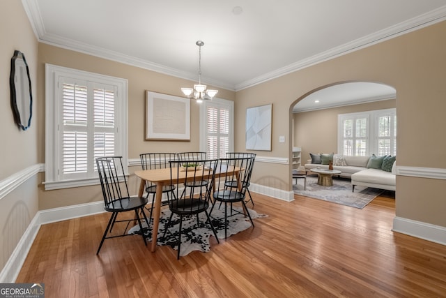 dining area with arched walkways, a chandelier, baseboards, wood finished floors, and ornamental molding