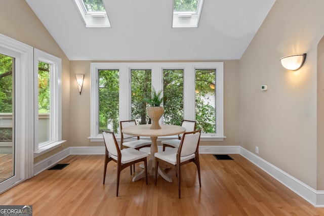 dining space with baseboards, visible vents, vaulted ceiling with skylight, and light wood-style floors