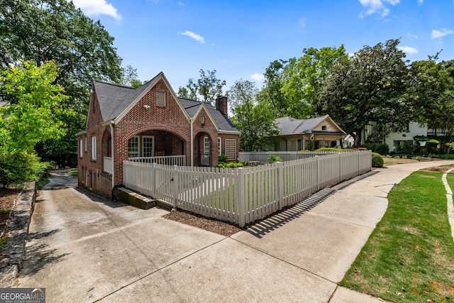 view of front of home featuring covered porch, a chimney, brick siding, concrete driveway, and a fenced front yard