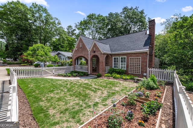tudor house featuring fence private yard, a garden, a front yard, a chimney, and brick siding