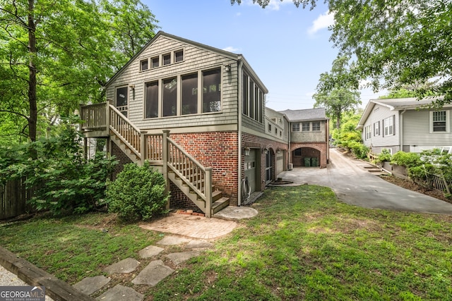 rear view of property with a lawn, stairs, concrete driveway, and brick siding