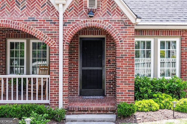 view of exterior entry featuring brick siding and a shingled roof