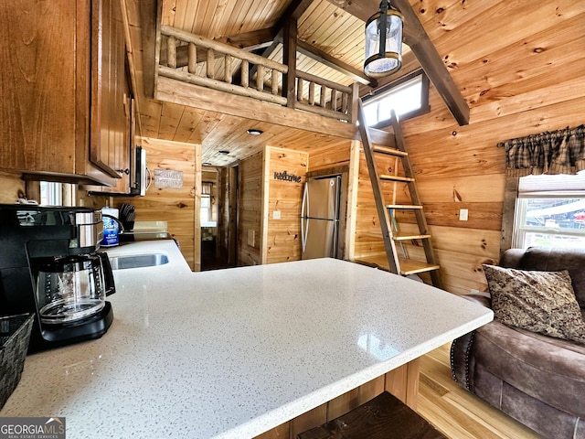 kitchen with freestanding refrigerator, a peninsula, wooden walls, and a wealth of natural light