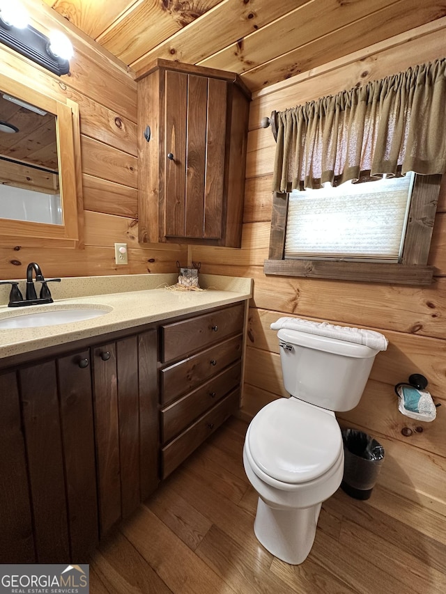 bathroom with wooden walls, toilet, wood finished floors, and vanity