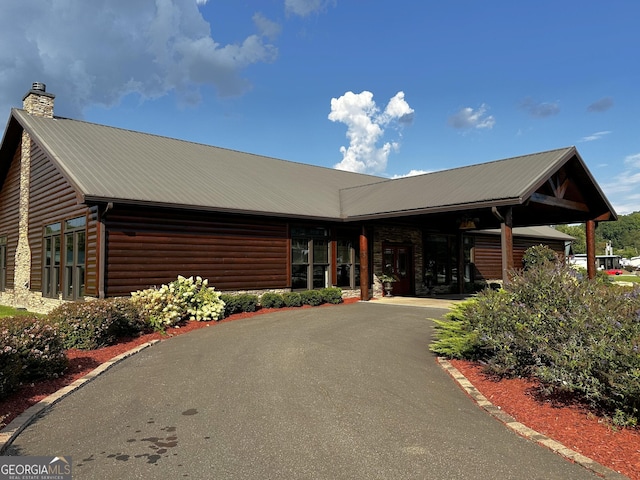 view of front of house with a chimney, log veneer siding, and metal roof