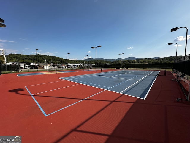 view of tennis court featuring a mountain view, community basketball court, and fence