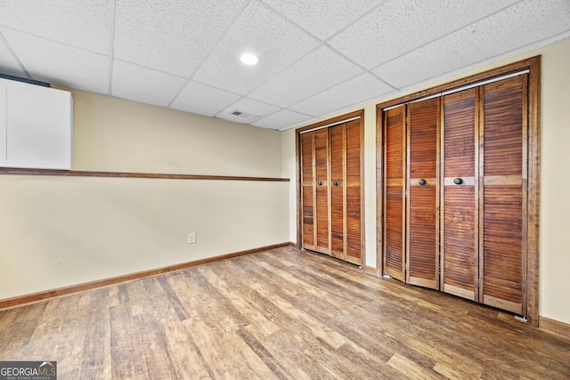 unfurnished bedroom featuring visible vents, wood finished floors, baseboards, two closets, and a drop ceiling