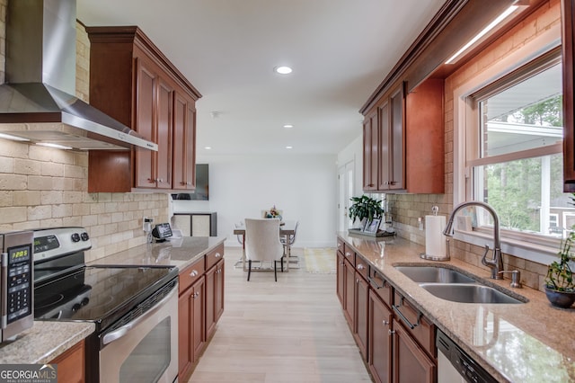 kitchen featuring a sink, appliances with stainless steel finishes, a healthy amount of sunlight, and wall chimney range hood