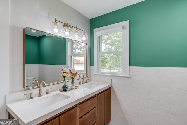 full bath with double vanity, tile walls, wainscoting, and a sink