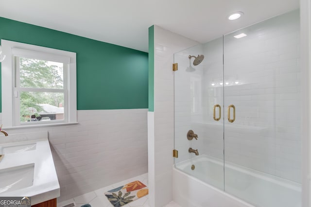 full bathroom with double vanity, wainscoting, tile walls, bath / shower combo with glass door, and a sink