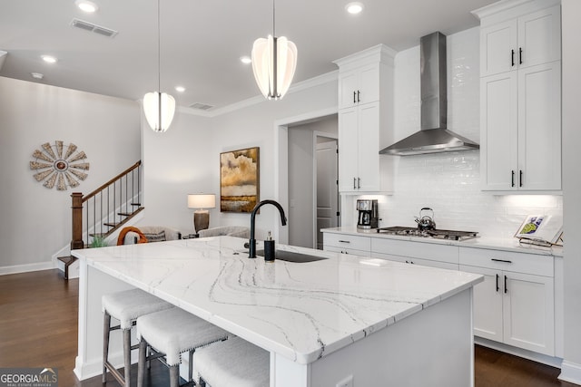 kitchen with visible vents, a sink, wall chimney exhaust hood, and decorative backsplash