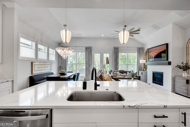 kitchen with a sink, a fireplace, open floor plan, lofted ceiling, and stainless steel dishwasher