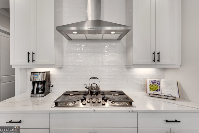 kitchen featuring wall chimney range hood, white cabinets, light stone countertops, and decorative backsplash