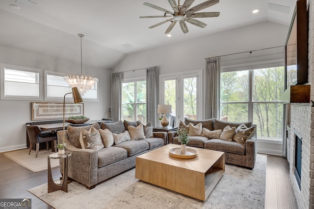 living area featuring a fireplace, ceiling fan with notable chandelier, recessed lighting, lofted ceiling, and light wood-type flooring