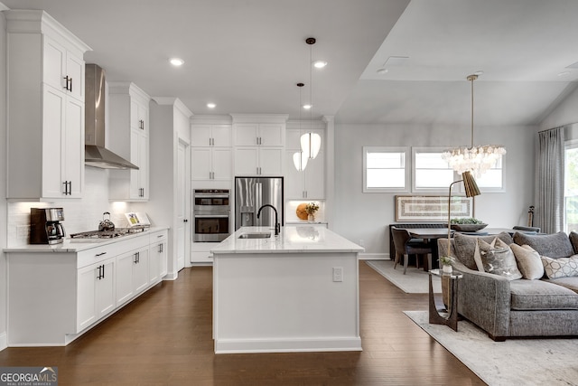 kitchen featuring wall chimney range hood, appliances with stainless steel finishes, white cabinetry, open floor plan, and tasteful backsplash