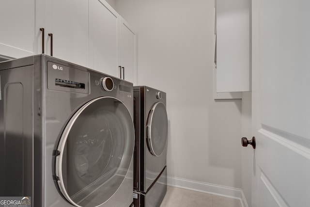 laundry room featuring cabinet space, baseboards, light tile patterned floors, and washing machine and clothes dryer
