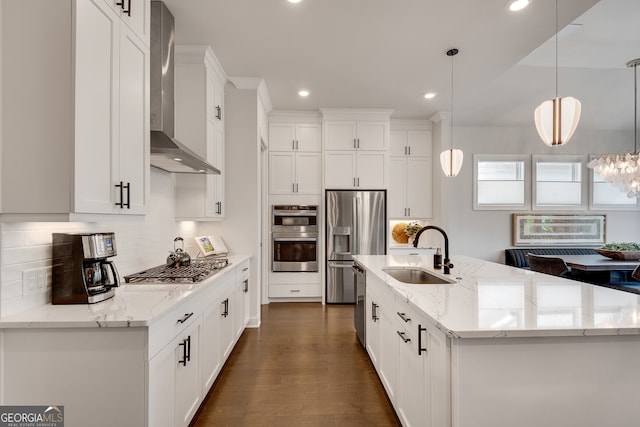 kitchen with decorative backsplash, wall chimney range hood, white cabinets, a sink, and appliances with stainless steel finishes